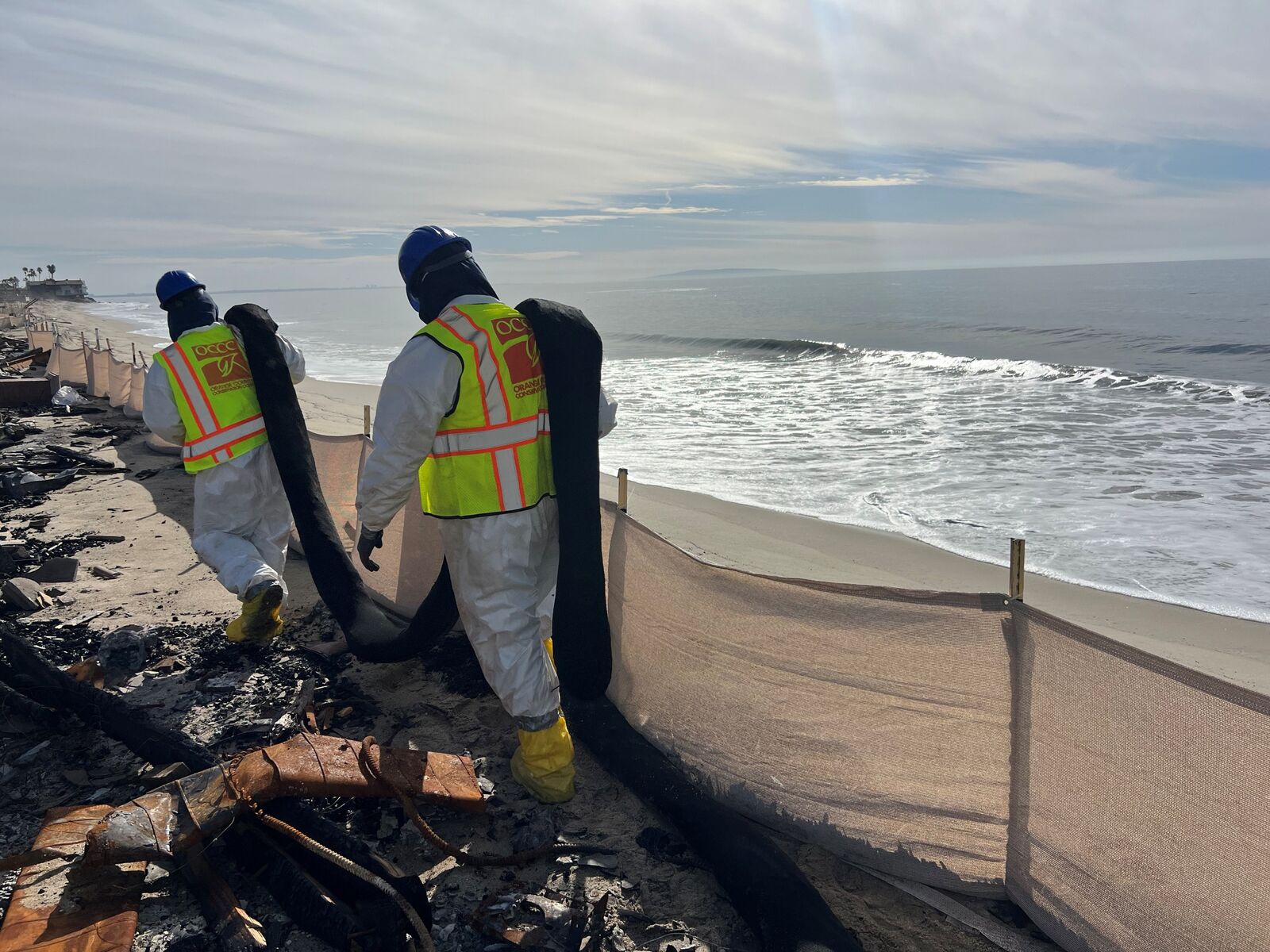 Crews in protective suits installing barriers during coastal fire recovery